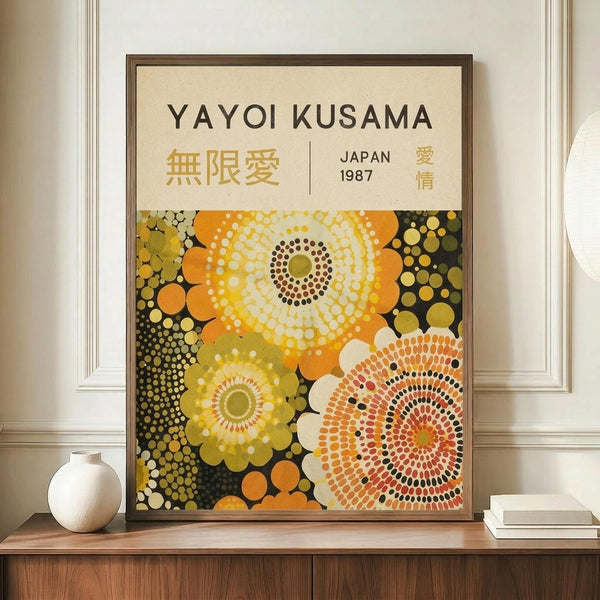 May include: Framed poster with abstract circular dot patterns in yellow, orange, and green tones displayed on wooden sideboard next to white ceramic vase and books. The artwork features large radiating circles made of dots in warm colors against dark background, shown in brown frame against cream walls with white molding.