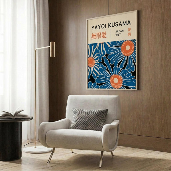 May include: Modern living room with cream armchair, geometric pillow, and gold floor lamp. Framed art poster on wood wall panel features blue and orange floral sunburst pattern with Japanese text. Natural lighting from window with curtains. Dark round side table with open book.