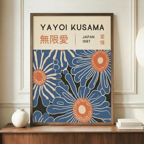 May include: Framed art print featuring blue stylized flowers with coral-orange centers and white dotted details on cream background, displayed on wooden sideboard next to white ceramic vase and stacked books against white paneled wall
