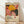 May include: Framed art print featuring vibrant abstract floral design with yellow dahlia, pink and coral organic shapes, black polka dot patterns, and radiating botanical forms. Poster displays "YAYOI KUSAMA" text and Japanese characters below colorful artwork. Natural wood frame sits on light wooden floor against white wall with soft window light creating diagonal shadows across the scene.