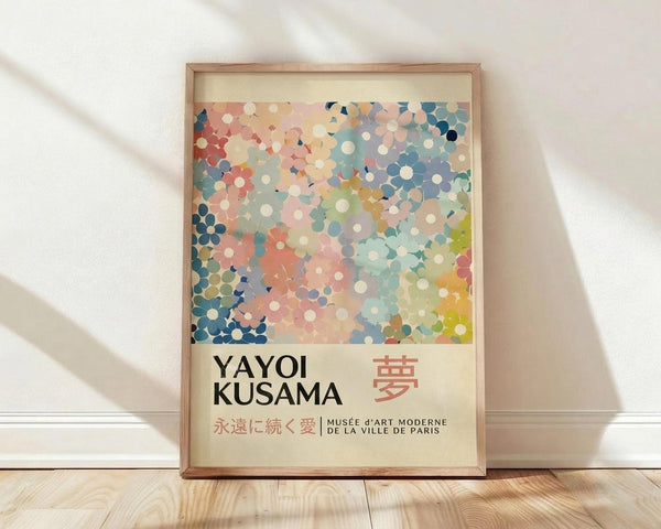 May include: Framed poster with colorful dotted abstract pattern in pink, blue, yellow and coral tones, featuring "YAYOI KUSAMA" text and Japanese characters below the artwork. Light wood frame leaning against white wall on wooden floor with soft natural lighting and shadows.