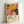 May include: A framed poster print featuring vibrant floral artwork with a large yellow flower, pink and coral blooms, and black polka-dotted shapes against a white background. The print displays "YAYOI KUSAMA" in bold black text with Japanese characters and "MUSEE D'ART MODERNE DE LA VILLE DE PARIS" below. The artwork is shown in a light wood frame, leaning against a white wall on what appears to be a light-colored surface.