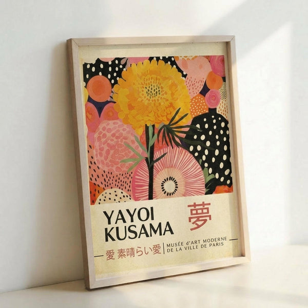 May include: A framed poster print featuring vibrant floral artwork with a large yellow flower, pink and coral blooms, and black polka-dotted shapes against a white background. The print displays "YAYOI KUSAMA" in bold black text with Japanese characters and "MUSEE D'ART MODERNE DE LA VILLE DE PARIS" below. The artwork is shown in a light wood frame, leaning against a white wall on what appears to be a light-colored surface.