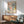May include: Framed art print with colorful dotted pattern in blues, pinks, and earth tones, displayed above wood credenza with white ceramic lamp. Modern mint green armchair with wooden frame sits nearby on wooden floor with natural sunlight streaming across white wall.