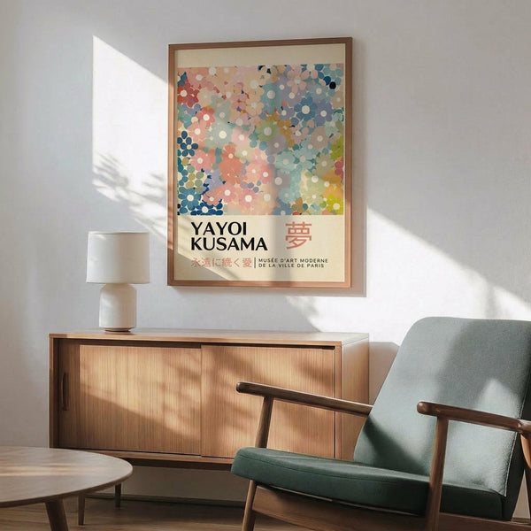 May include: Framed art print with colorful dotted pattern in blues, pinks, and earth tones, displayed above wood credenza with white ceramic lamp. Modern mint green armchair with wooden frame sits nearby on wooden floor with natural sunlight streaming across white wall.