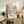 May include: Framed art print with colorful abstract polka dot pattern in pastel blues, pinks, and yellows, displayed on rustic wooden sideboard next to fern plant, ceramic vase, and stacked books in neutral-toned living room with cream upholstered furniture