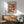 May include: Colorful mushroom artwork poster displayed in modern living room with wooden sideboard, mint green armchair, and white lamp. The framed print features vibrant polka-dotted mushrooms in red, orange, pink, and green tones against dark background. Sunlight streams across white wall creating geometric shadows. Mid-century modern furniture with clean lines and natural wood finishes complement the artistic wall decor.
