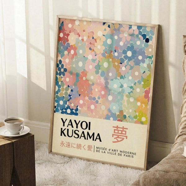 May include: Framed poster with colorful polka dot pattern in blues, pinks, corals, and greens displayed in bright room corner. White teacup on wooden block nearby, cream textured rug below, beige blanket draped beside frame. Text shows "YAYOI KUSAMA" with Japanese characters and "MUSEE d'ART MODERNE DE LA VILLE DE PARIS" in clean typography on cream background beneath dotted artwork.