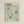 May include: Framed museum exhibition poster featuring abstract organic shapes in soft turquoise and teal tones against cream background. Design shows dotted patterns, radiating burst forms, and flowing circular elements. Text displays "YAYOI KUSAMA" in bold black letters with Japanese characters, "1991" date, and "MUSEUM OF MODERN ART NEW YORK EXHIBITION ART" at bottom. Light wood frame hangs on white wall.