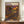 May include: Framed exhibition poster with colorful polka dot pattern in vibrant oranges, purples, and yellows against dark background, displayed on wooden sideboard next to white ceramic vase and stack of books in elegant room with cream walls and white trim molding.