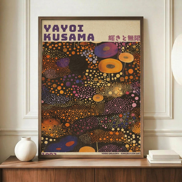 May include: Framed exhibition poster with colorful polka dot pattern in vibrant oranges, purples, and yellows against dark background, displayed on wooden sideboard next to white ceramic vase and stack of books in elegant room with cream walls and white trim molding.