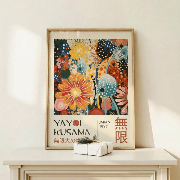 May include: Framed art poster with colorful abstract floral design featuring large orange and yellow blooms, polka-dotted patterns in blues and greens, displayed on light wood console table next to small wrapped gift with twine and greenery sprig against cream wall