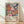 May include: Framed art print featuring vibrant floral pattern with large pink, coral, and blue stylized flowers against dark navy background. Text reads "YAYOI KUSAMA" and "JAPAN 1987" with Japanese characters below. Light wood frame sits on wooden floor against white wall with soft natural lighting creating diagonal shadows.