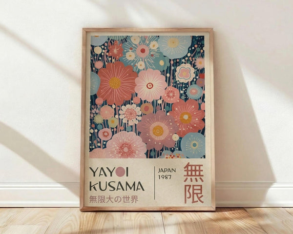 May include: Framed art print featuring vibrant floral pattern with large pink, coral, and blue stylized flowers against dark navy background. Text reads "YAYOI KUSAMA" and "JAPAN 1987" with Japanese characters below. Light wood frame sits on wooden floor against white wall with soft natural lighting creating diagonal shadows.