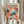 May include: Person holding framed poster featuring abstract art with colorful polka dot patterns in coral, teal, navy, and pink tones. Wave-like motifs flow across bottom. Museum of Modern Art New York text visible at bottom. Natural wood frame against white curtained background with dried pampas grass stems visible on left side.
