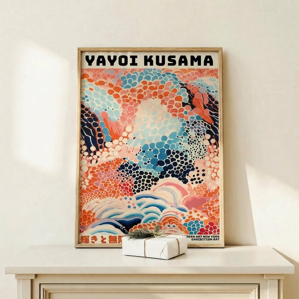 May include: Framed art print leaning against white wall on light wood console table with small white gift box. Poster features abstract design with colorful dotted patterns in coral, blue, navy, and pink resembling organic cellular forms and flowing waves. Bold black text at top, natural wood frame, modern minimalist room setting.