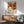 May include: Framed Yayoi Kusama exhibition poster with colorful polka-dotted flowers and circular patterns in orange, brown, and cream tones, displayed above a wooden sideboard with white lamp in modern living room setting with mint green armchair