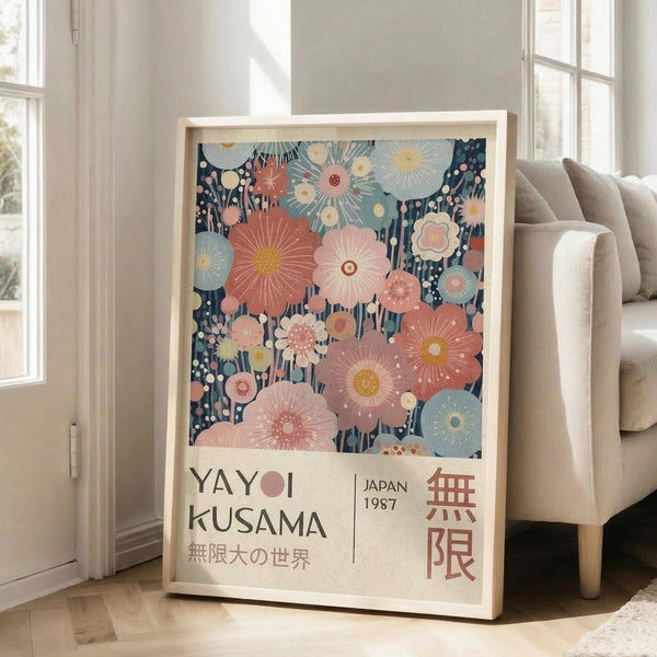 May include: Framed art print featuring stylized floral design with coral, pink, and blue blooms on dark navy background, displayed against white wall next to beige upholstered sofa. Print shows Japanese text and "JAPAN 1987" with decorative flower motifs in soft pastel colors. Light wooden frame complements bright, airy living room setting with large windows.