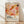 May include: Abstract art poster in wooden frame leaning against white wall on light wood floor. Artwork features organic flowing shapes in warm tones of coral, orange, pink, yellow and burgundy with scattered dots. Bottom text reads "YAYOI KUSAMA" with Japanese characters and "MUSÉE D'ART MODERNE DE LA VILLE DE PARIS". Soft natural lighting creates diagonal shadows across textured white wall.