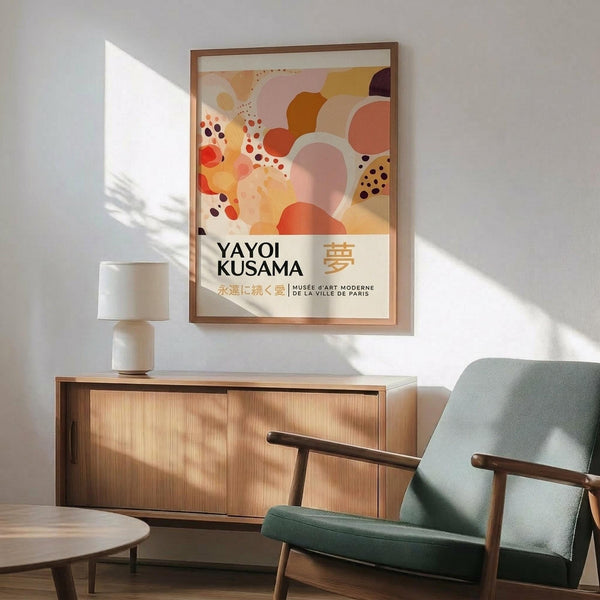 May include: Framed abstract art poster with warm orange, pink, and coral circular shapes and polka dot patterns, displayed above a wooden sideboard with ceramic lamp. Mid-century modern living room setting features sage green upholstered chair with wooden arms, round coffee table, and natural sunlight creating geometric shadows on white walls.