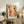 May include: Framed abstract art poster with organic shapes in coral, orange, brown, and cream colors featuring dots, circles, and botanical elements, displayed on rustic wooden sideboard next to fern plant, ceramic vase, and stacked books in warm-toned living room setting.