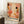 May include: Framed abstract art print featuring warm coral, orange, and cream organic shapes with black dots, botanical elements, and Japanese text reading "Yayoi Kusama" and "Osaka." Print leans against white wall next to wooden side table with coffee cup and cozy blanket in softly lit room setting.