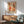 May include: Framed abstract art print featuring warm coral, orange, and beige organic shapes with black dots and botanical elements, displayed above a wooden sideboard with white lamp in modern living room with mint green mid-century chair and natural lighting creating geometric shadows on white wall.