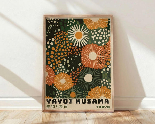 May include: Framed art print with colorful abstract floral design featuring radiating sunburst patterns in orange, green, and cream against dark background. Japanese text reads "Yayoi Kusama" and "Tokyo" at bottom. Natural wood frame displays against white wall on light wooden floor with soft shadows.