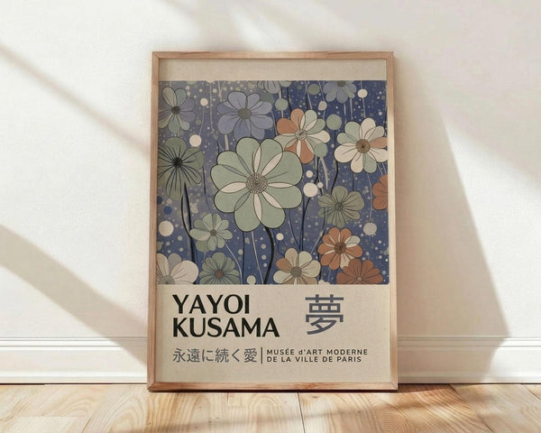 May include: Framed art print leaning against white wall on light wood floor. The poster features stylized flowers in muted greens, blues, and coral tones against a dark blue dotted background. Text at bottom reads "YAYOI KUSAMA" with Japanese characters and "MUSEE d'ART MODERNE DE LA VILLE DE PARIS". Natural wood frame with light matting. Soft window light creates diagonal shadows across the white textured wall.