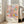 May include: Framed exhibition poster featuring colorful abstract floral design with pastel pink, blue, yellow and orange flowers and polka dot patterns, displayed against white wall next to beige sofa in bright living room with large windows and natural lighting