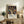 May include: Framed poster with colorful abstract art featuring flowing tree-like forms with multicolored dots and circles on black background, displaying "YAYOI KUSAMA" text below artwork. Light wood frame sits on rustic wooden sideboard alongside fern plant, books, and ceramic vase in bright modern living room setting with beige furniture and white walls.