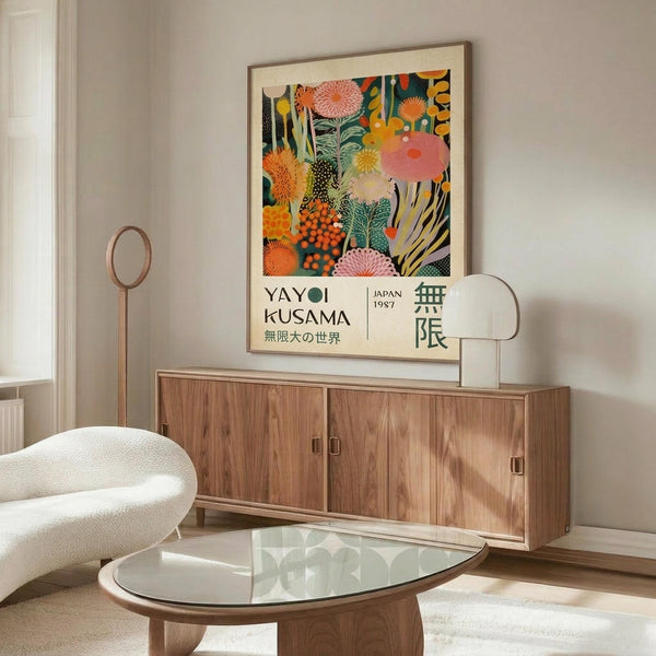 May include: Yayoi Kusama exhibition poster mockup in modern living room setting with warm beige walls. Colorful botanical artwork features vibrant flowers, plants and abstract patterns in orange, pink, green and yellow tones. Poster displayed in thin wooden frame above mid-century walnut sideboard. Room includes white curved lounge chair, glass-top oval coffee table, and brass floor lamp creating bright, contemporary interior design.