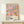 May include: Framed colorful floral art print leaning against white wall on light wood surface. Artwork features pastel pink, blue, orange and green abstract flowers with polka dots. Small white gift box with twine sits in front of frame. Print shows exhibition text reading "YAYOI KUSAMA" and "MUSEE d'ART DE PARIS" with dates "28. APRIL - 14. MAI 1984". Light wood frame complements minimal neutral decor setting.