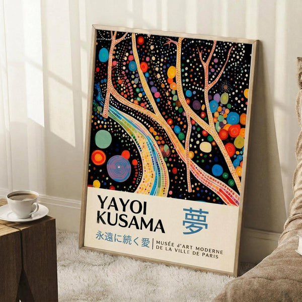 May include: Framed poster with black background featuring colorful polka dots and flowing curved lines in rainbow colors, displayed leaning against white wall corner next to white coffee cup on wooden surface and beige textile, showcasing Yayoi Kusama exhibition artwork with Japanese text and museum attribution at bottom