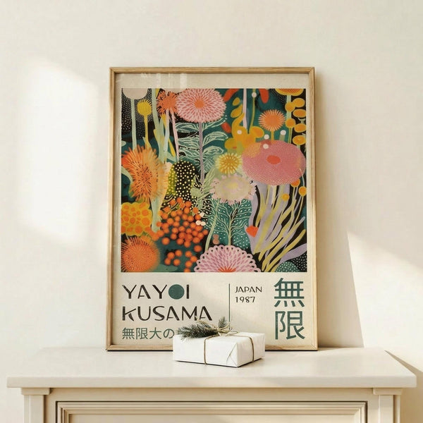 May include: Framed poster with vibrant botanical illustration featuring colorful abstract flowers, mushrooms, and organic shapes in orange, pink, green, and yellow tones. Text reads "YAYOI KUSAMA JAPAN 1987" with Japanese characters. Displayed on light wood console with small wrapped gift box. Natural wood frame against cream wall in minimalist room setting.