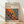 May include: Framed poster print leaning against white wall on light wooden floor. The artwork features Yayoi Kusama's signature polka dot style in vibrant red, orange, yellow, and blue colors with flowing organic shapes and circular patterns. Japanese text appears at top along with "JAPAN 1987". Natural wooden frame surrounds the cream-colored poster. Soft natural lighting creates gentle shadows on the white textured wall.