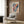 May include: Colorful abstract art poster with flowing waves, dots, and organic shapes in blues, oranges, and pinks, displayed in light wood frame on wood paneled wall above beige upholstered armchair with geometric patterned pillow, brass floor lamp, and dark round side table with open book in modern neutral-toned room.