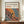 May include: Framed poster print featuring abstract flowing patterns with colorful dots and organic shapes in red, orange, yellow, and blue tones. Japanese characters and "JAPAN 1987" text appear at top. Brown wooden frame sits on light wood console table beside white ceramic vase and stacked books against cream paneled wall.