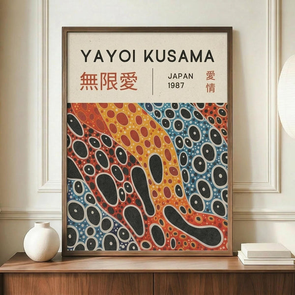 May include: Framed poster print featuring abstract flowing patterns with colorful dots and organic shapes in red, orange, yellow, and blue tones. Japanese characters and "JAPAN 1987" text appear at top. Brown wooden frame sits on light wood console table beside white ceramic vase and stacked books against cream paneled wall.