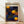 May include: Framed poster print leaning against white wall on light wood floor. The artwork features a deep blue background with scattered orange and yellow polka dots of varying sizes, three prominent orange spiral circles resembling suns or flowers, and text reading "Yayoi Kusama" with Japanese characters and "Kyoto" at top. Natural wood frame surrounds the vibrant abstract composition in contemporary room setting.