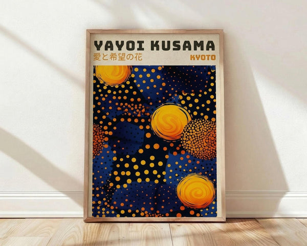 May include: Framed poster print leaning against white wall on light wood floor. The artwork features a deep blue background with scattered orange and yellow polka dots of varying sizes, three prominent orange spiral circles resembling suns or flowers, and text reading "Yayoi Kusama" with Japanese characters and "Kyoto" at top. Natural wood frame surrounds the vibrant abstract composition in contemporary room setting.