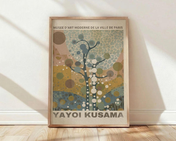 May include: Framed poster with abstract tree design featuring colorful circles and dots in earth tones - blues, greens, browns, and yellows. The artwork shows a stylized tree with branching patterns and polka dot elements against a textured background. Text at top reads "Musee d'Art Moderne de la Ville de Paris" and "Yayoi Kusama" at bottom. Natural wood frame sits on light wooden floor against white wall with soft natural lighting.