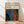 May include: Framed poster print with cream background featuring "YAYOI KUSAMA" in black text, orange Japanese characters, and "JAPAN 1987" with red characters. Bottom half shows abstract artwork with flowing blue and red organic shapes surrounded by colorful dots in white, orange, yellow and green on black background. Natural wood frame sits on light wooden floor against white wall with soft shadows.
