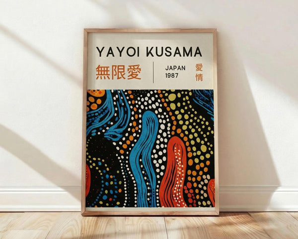 May include: Framed poster print with cream background featuring "YAYOI KUSAMA" in black text, orange Japanese characters, and "JAPAN 1987" with red characters. Bottom half shows abstract artwork with flowing blue and red organic shapes surrounded by colorful dots in white, orange, yellow and green on black background. Natural wood frame sits on light wooden floor against white wall with soft shadows.