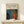 May include: Framed poster print featuring Yayoi Kusama-inspired artwork with vibrant polka dot patterns in blue, red, orange, and yellow against black background, flowing organic shapes, Japanese text, "JAPAN 1987" marking. Light wood frame displayed on minimal white wooden console table with small wrapped gift box beside it, white wall background.