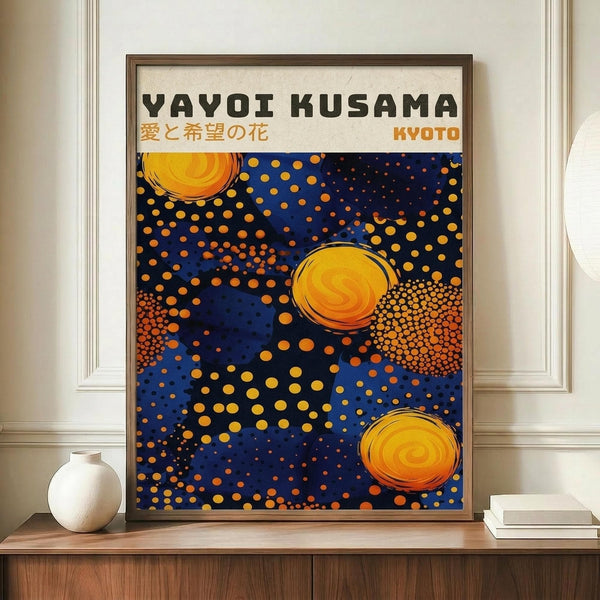 May include: Framed art poster with blue background and orange polka dot patterns, featuring three circular spiral designs in yellow and orange. Japanese text visible at top. Displayed on wooden sideboard next to white ceramic vase and stacked books against cream colored wall with white trim molding.