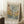 May include: Framed art poster leaning against white wall corner on fluffy white rug next to wooden side table with coffee cup. Poster features abstract tree design with colorful polka dots and circles in blues, greens, yellows, and earth tones. Text reads "Musee d'Art Moderne de la Ville de Paris" at top and "Yayoi Kusama" at bottom. Light wood frame, cozy beige blanket visible at right edge.