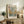 May include: Framed art print featuring abstract tree design with colorful dots and circles in earth tones, displayed on rustic wooden sideboard alongside fern plant, ceramic vase, and books in cozy living room setting with neutral walls and beige furniture.