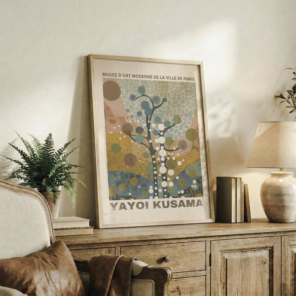 May include: Framed art print featuring abstract tree design with colorful dots and circles in earth tones, displayed on rustic wooden sideboard alongside fern plant, ceramic vase, and books in cozy living room setting with neutral walls and beige furniture.
