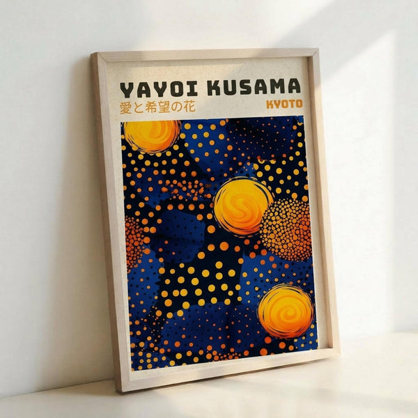 Framed poster featuring Yayoi Kusama-inspired artwork with bright yellow and orange circular forms scattered across a deep blue background. The composition includes dotted patterns in various sizes creating a cosmic, polka-dot design. Text at top reads "YAYOI KUSAMA" in black letters with Japanese characters below and "KYOTO" in orange. The poster is displayed in a light wooden frame leaning against a white wall.